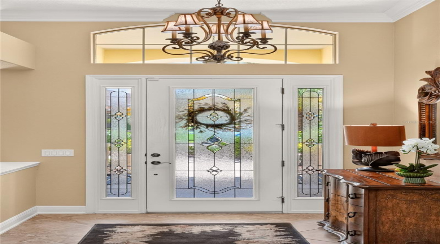 Inside The Foyer, The Full Length Leaded Glass Insert Front Door W/ Matching Sidelites And Arched Transom Serve As A Backdrop For The Ornate Chandelier Hanging From The 12' Ceiling. A Half Wall (R) Perfectly Frames The View Of The Formal Dining Room. Note Unique 3 Drawer Chest (R) Manufactured By Palmer Home.