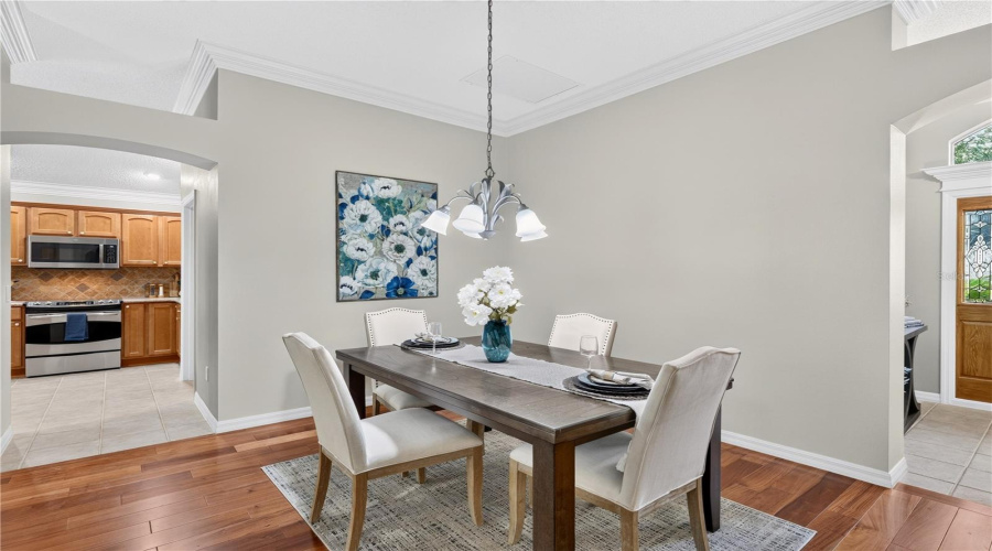 Dining Area With Elegant Lighting, Wood Flooring, And Convenient Access To The Kitchen Through The Arched Opening.