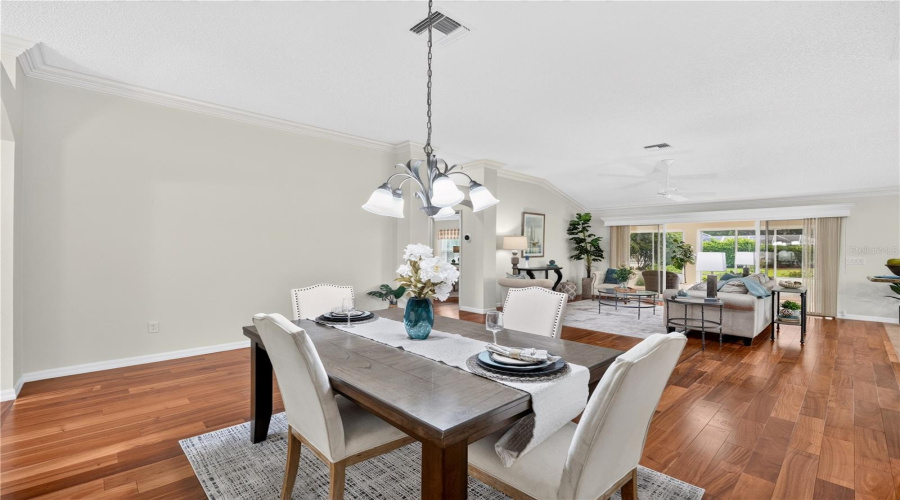 Formal Dining Space With Rich Wood Flooring, Neutral Wall Color, And An Open Sightline Into The Living Room.