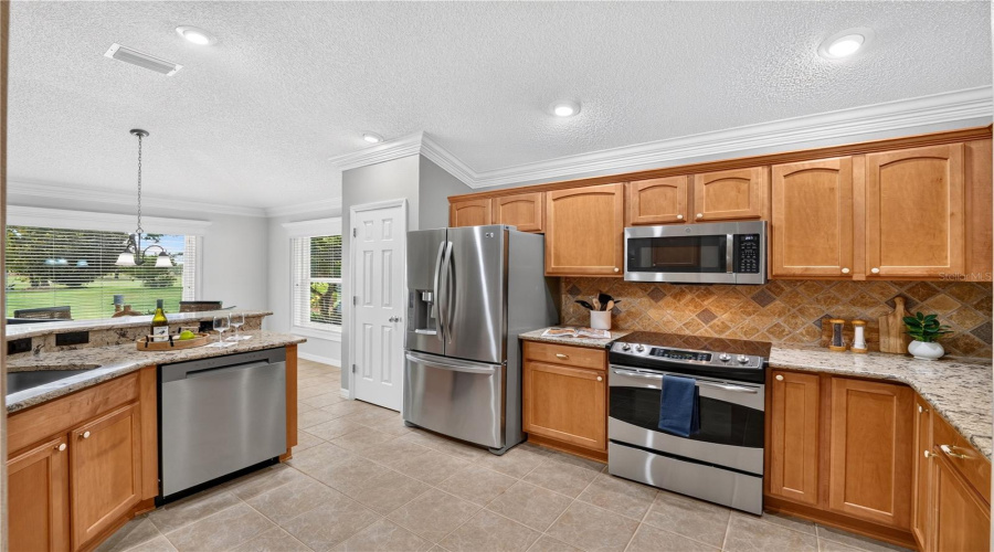Well-Appointed Kitchen With Wood Cabinetry, Stainless Steel Appliances, Tile Backsplash, And Ample Counter Space.
