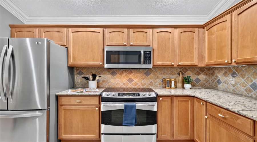 Kitchen Detail Featuring High End Stainless Steel Appliances, Warm Wood Cabinetry, Tile Backsplash, And Recessed Lighting.