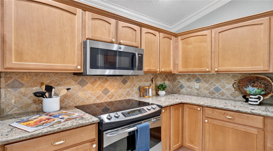 Functional Kitchen Layout With Generous Cabinet Storage, Neutral Countertops, And A Decorative Tile Backsplash.