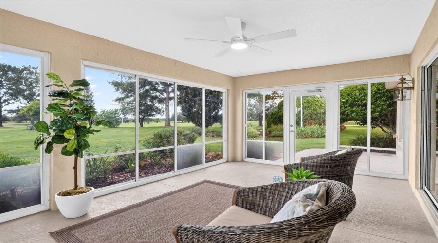 Spacious Enclosed Lanai With Tile Flooring, Ceiling Fan, And Walls Of Windows Overlooking The Peaceful Green Space.