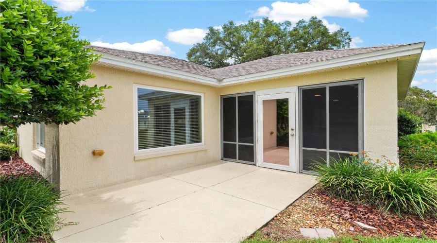Rear Patio Area With Access From The Enclosed Lanai, Surrounded By Mature Landscaping And Easy Outdoor Living Space.