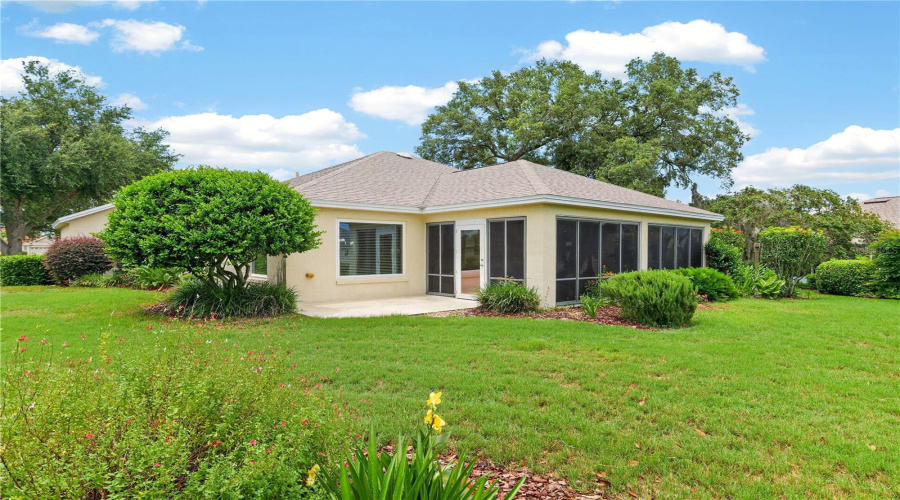 Rear Exterior View Highlighting The Enclosed Lanai, Spacious Lawn, And Serene Golf Course-Style Setting.
