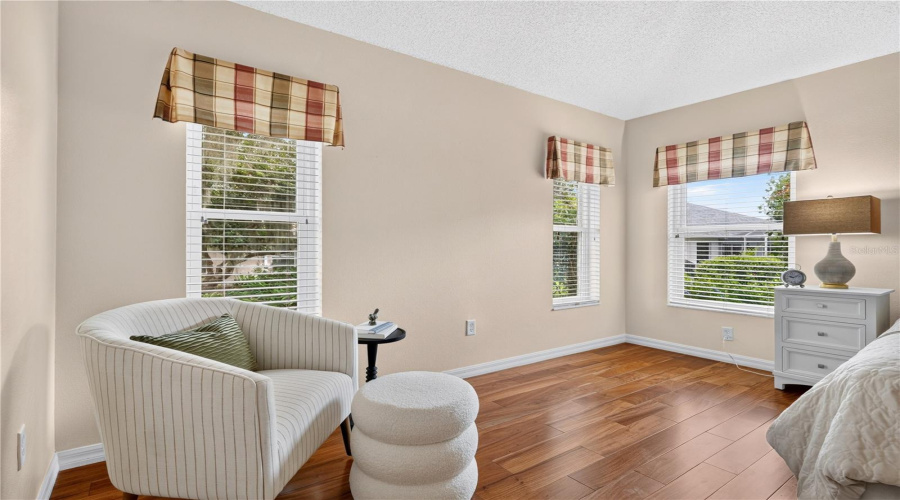 Comfortable Sitting Area Within The Primary Bedroom, Framed By Bright Windows And Peaceful Outdoor Views.