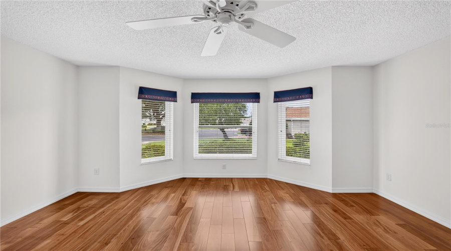 Bright Guest Bedroom Featuring Multiple Windows, Neutral Walls, Wood Flooring, And Peaceful Outdoor Views.