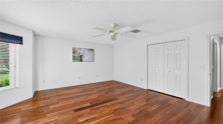 Guest Bedroom With Wood Flooring, Ceiling Fan, Closet Storage, And A Clean, Neutral Design.