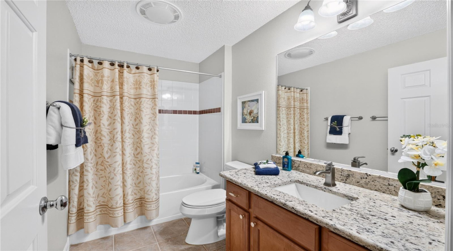 Guest Bathroom With Tub/Shower Combination, Quartz Counter, Wood Vanity, Large Mirror, And Neutral Finishes.