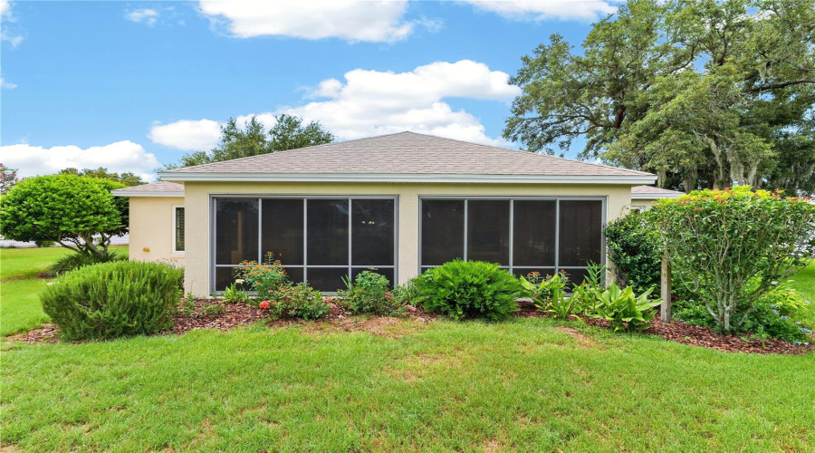 Rear Exterior View Highlighting The Enclosed Lanai, Mature Landscaping, And Beautifully Maintained Lawn.