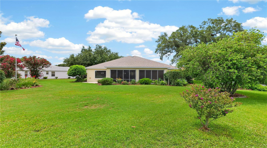 Wide Backyard View Highlighting The Enclosed Lanai, Generous Lawn Area, And Attractive Surrounding Landscapin