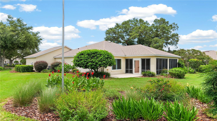 Beautiful Rear Exterior With Lush Lawn, Mature Plantings, And Colorful Garden Beds Framing The Home.