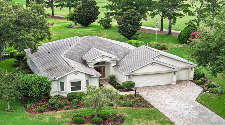 Elevated Front View Highlighting The Home’s Curb Appeal, Lush Greenery, And Desirable Lot Position Surrounded By Mature Trees.