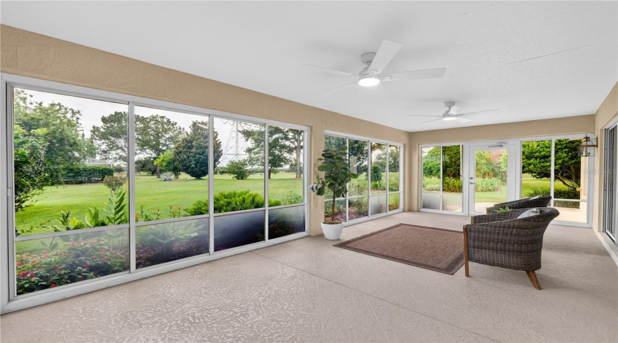 Enclosed Lanai With Walls Of Windows, Ceiling Fan, And Serene Views Of The Lush Landscaping And Open Green Space.