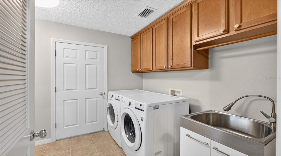Interior Laundry Room With Washer And Dryer, Upper Cabinetry, Utility Sink, And Convenient Storage.