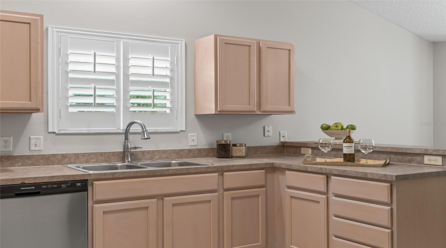Kitchen Sink Area With Plantation-Shuttered Window Above, Generous Cabinetry, And Plenty Of Counter Space For Food Preparation And Everyday Use.