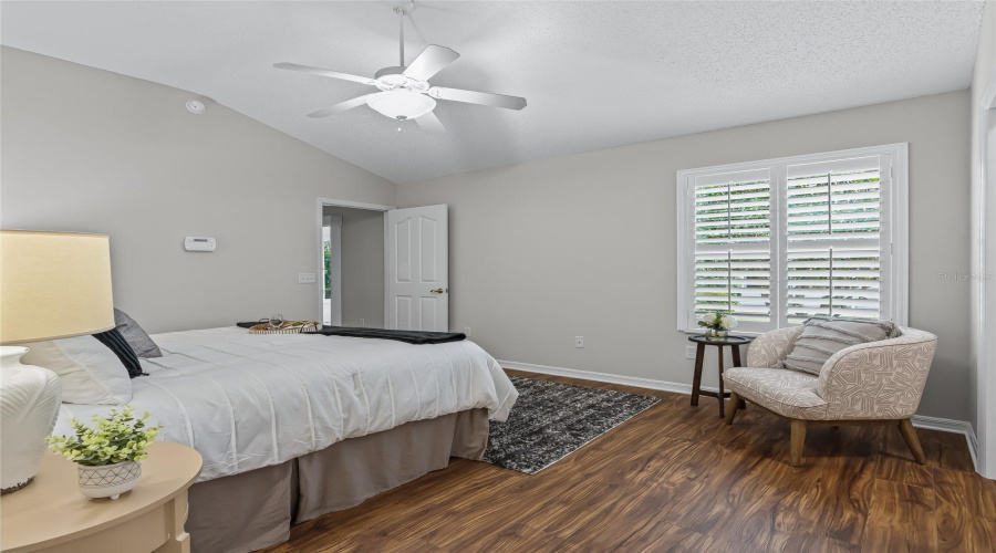 Spacious Primary Bedroom With Plantation Shutters, Ceiling Fan, Newer Wood-Look Lvp Flooring, And A Comfortable Sitting Area Near The Windows.