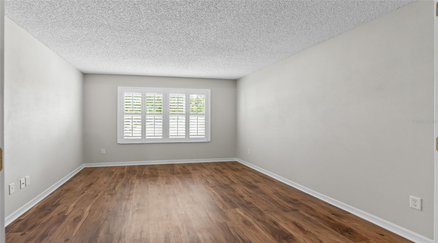 Bright Guest Bedroom Or Multi-Purpose Room With Newer Wood-Look Lvp Flooring, Plantation Shutters, And Neutral Finishes—An Inviting Space For Visiting Family And Friends.