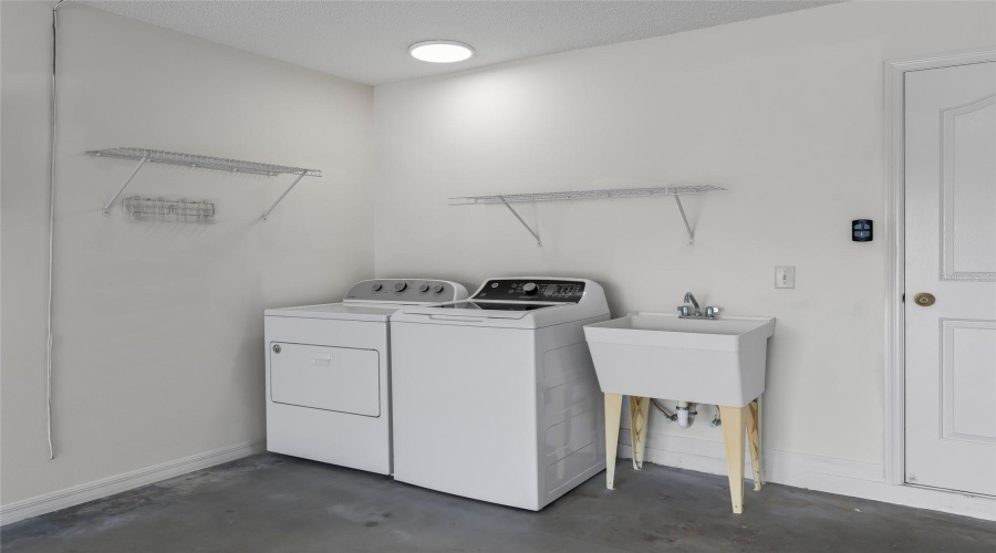 Garage Laundry Area Includes Washer And Dryer, Utility Sink, Shelving, And Additional Space For Household Storage.