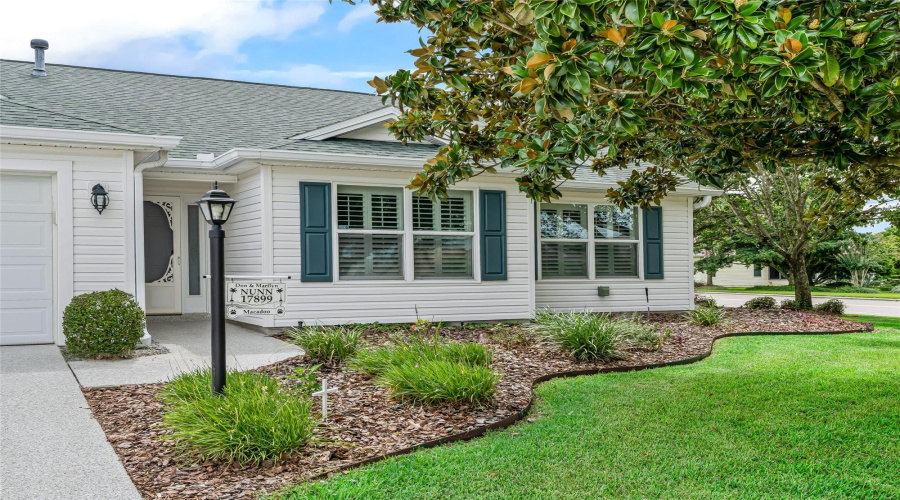 Charming Front Entry Accented By Mature Landscaping, Decorative Shutters, And A Covered Approach That Creates A Warm Welcome For Guests.