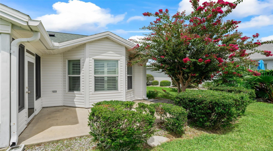 Attractive Rear Exterior With Mature Shrubs, Flowering Landscaping, And A Nicely Sized Patio For Enjoying The Florida Outdoors.