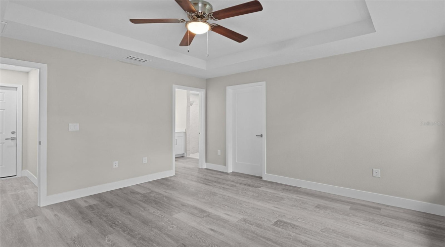 Primary Bedroom With Walk-In Closet On The Right, Ensuite Bathroom In The Center, And Bedroom Entry Door To The Far Left. The Door Leading Into The Garage Is Visible Through The Bedroom Doorway.