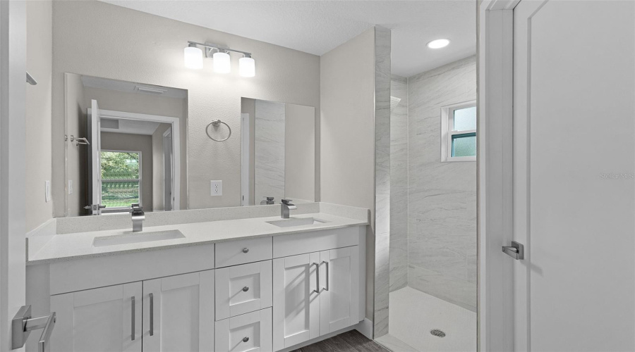 Primary Bathroom With Dual Sinks, Quartz Countertop, Sunken Tiled Shower, And Separate Toilet Room