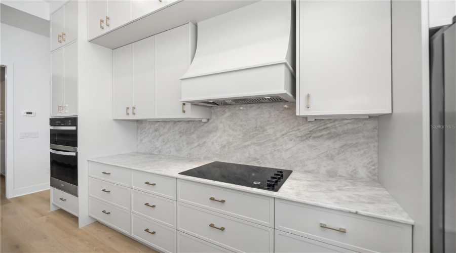 Kitchen Featuring Quartz Backsplash, Custom Range Hood And Double-Stacked Cabinetry.