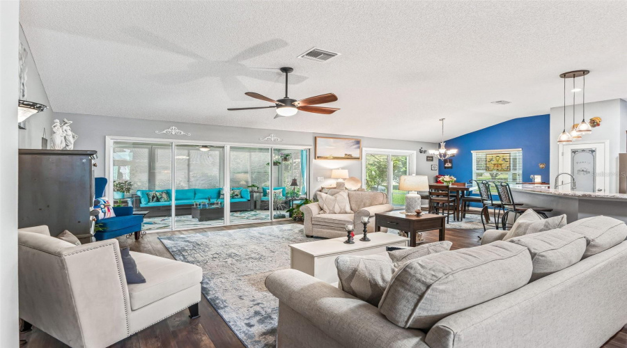 Expansive Living Room Offers Comfortable Seating Space, A Vaulted Ceiling, Ceiling Fan, And Abundant Natural Light From The Rear Windows And Glass Doors.