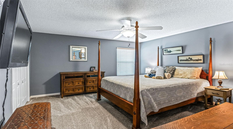 Comfortable Guest Bedroom Features Soft Carpeting, A Ceiling Fan, Neutral Décor, And Multiple Windows That Bring In Natural Light.