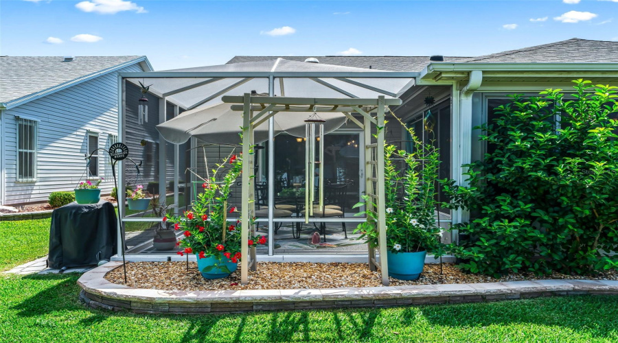 The Rear Exterior Features A Partially Enclosed Lanai With Two Adjoining Covered Birdcages- Both Patios Are Surrounded By Mature Landscaping And Colorful Plantings.