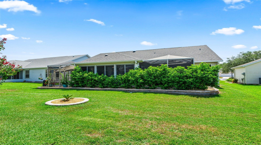 The Home’s Rear Elevation Showcases A Large Screened Living Area Bordered By Lush Hedges And A Beautifully Maintained Lawn.