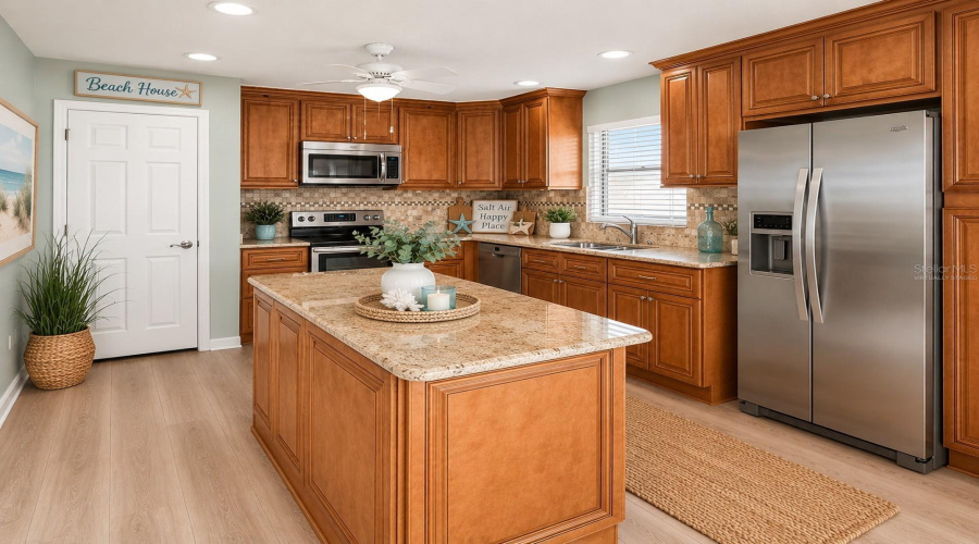 •  Kitchen: Virtually Staged – Coastal-Inspired Kitchen Featuring The Existing Cabinetry, Granite Countertops And Backsplash, With Added Décor And Refrigerator.