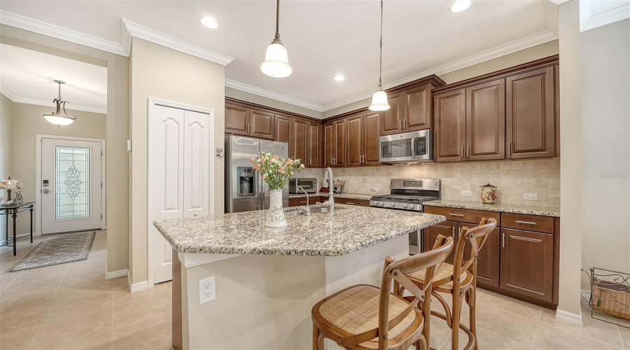 Rich Espresso Cabinetry, Granite Countertops, Stone Tile Backsplash, And Stainless Steel Appliances