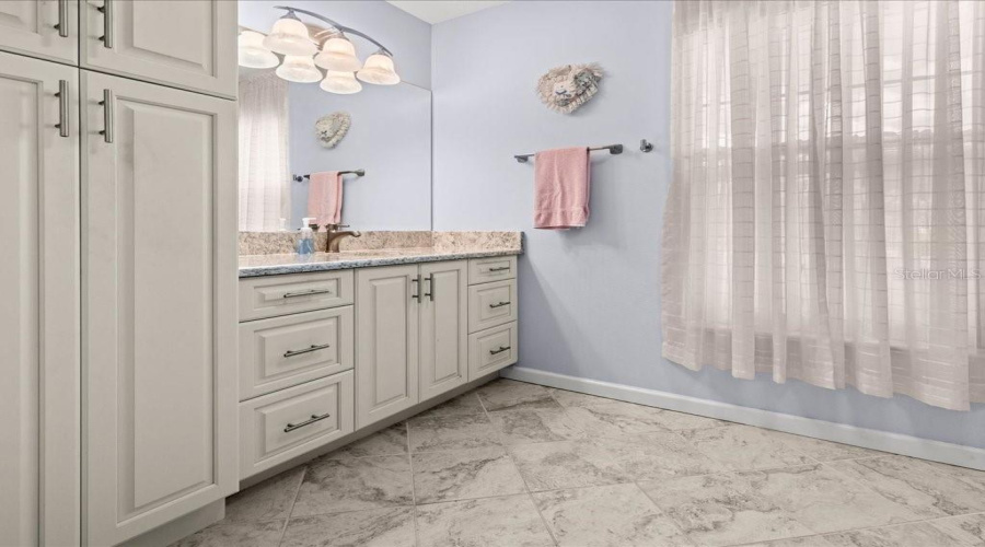 The Updated Primary Bathroom Has Large Single Sink Vanity With Linen Cabinet And Tile Floor.