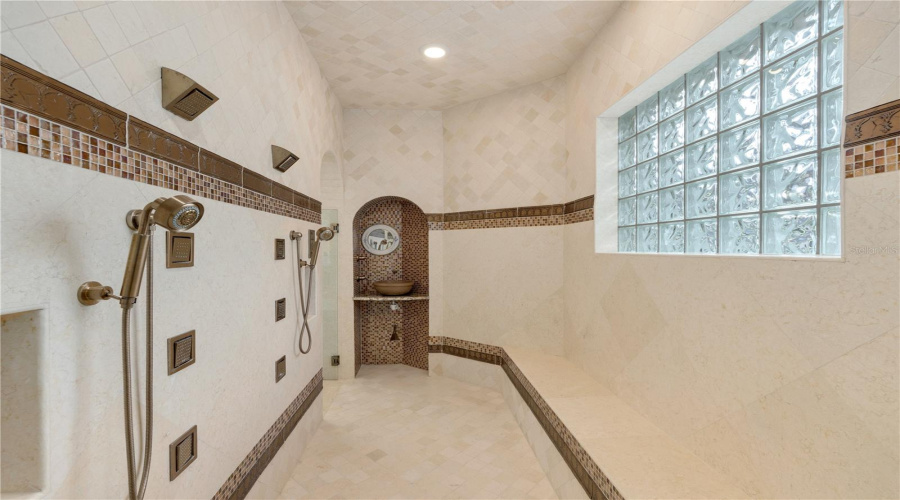 The Oversized Walk-In Shower Creates A True Spa Experience With Multiple Shower Fixtures, Decorative Stone Detailing And Softly Filtered Natural Light.