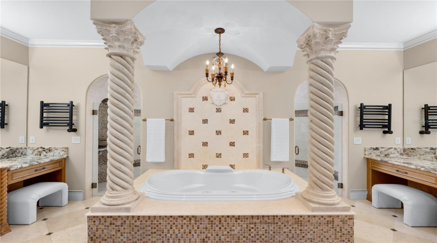 A Spa-Inspired Primary Bath Is Centered Around An Elevated Jacuzzi Soaking Tub Framed By Decorative Columns And Beautifully Appointed Dual Vanity Areas.