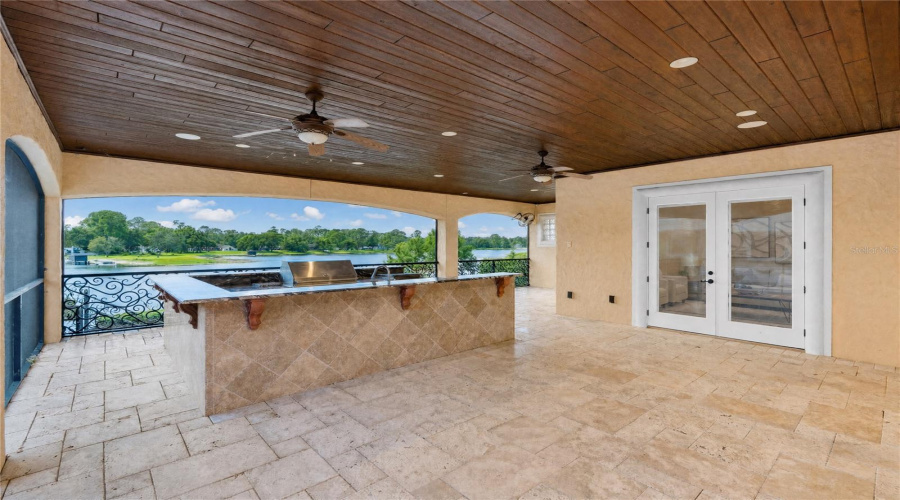 An Exceptional Lakefront Entertaining Terrace Offers A Covered Summer Kitchen With Viking Professional Grill And Alfresco Versapower Side Burner, Travertine Flooring And Sweeping Views Across Lake Mary.