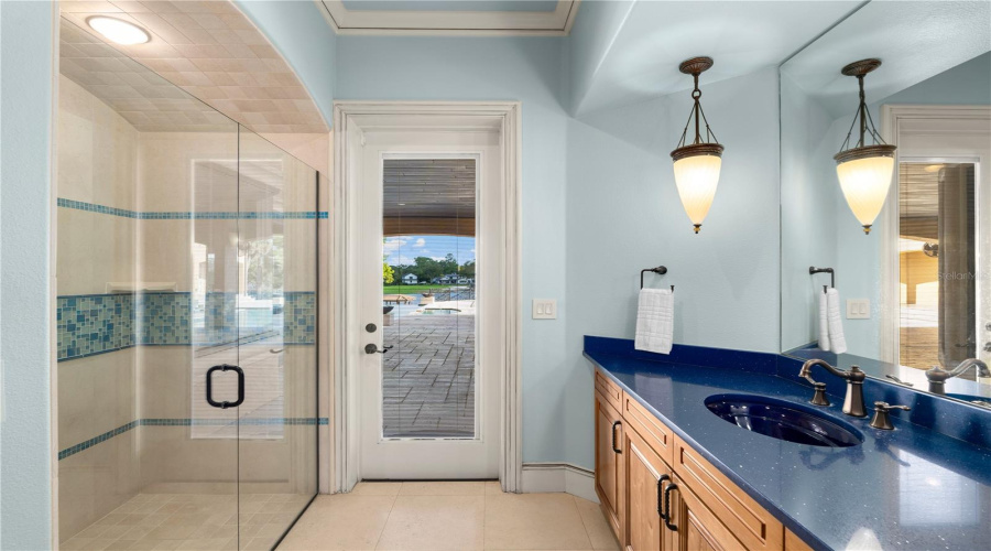 A Beautifully Finished Pool Bath Features A Glass-Enclosed Walk-In Shower, Custom Wood Vanity And Refined Tile Work.