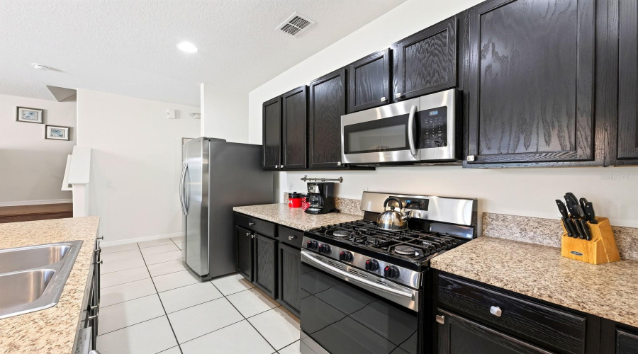 The Well-Appointed Kitchen Features Plenty Of Cabinet And Counter Space, A Large Island With Breakfast Bar Seating And Stainless Steel Appliances, Including A Gas Stove.