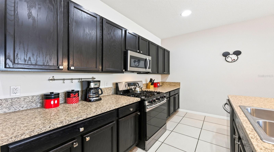 The Well-Appointed Kitchen Features Plenty Of Cabinet And Counter Space, A Large Island With Breakfast Bar Seating And Stainless Steel Appliances, Including A Gas Stove.