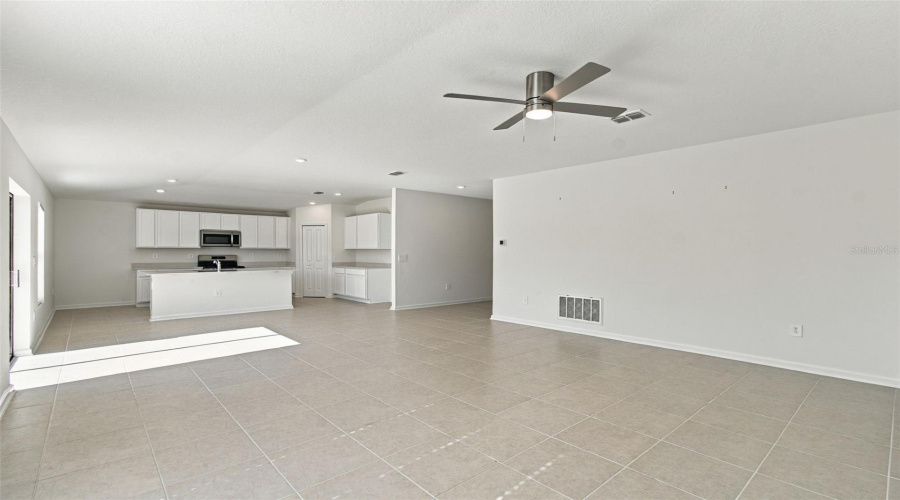 The Kitchen Offers A Spacious Island With Breakfast Bar, White Shaker-Style Cabinetry, And Quartz Countertops, All Overlooking The Dining And Living Areas.