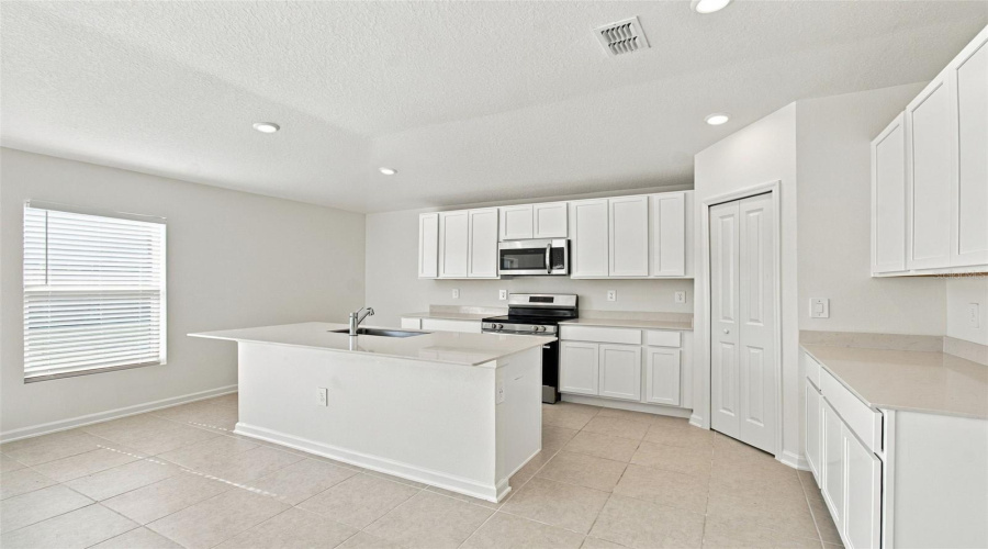 The Kitchen Offers A Spacious Island With Breakfast Bar, White Shaker-Style Cabinetry, And Quartz Countertops, All Overlooking The Dining And Living Areas.