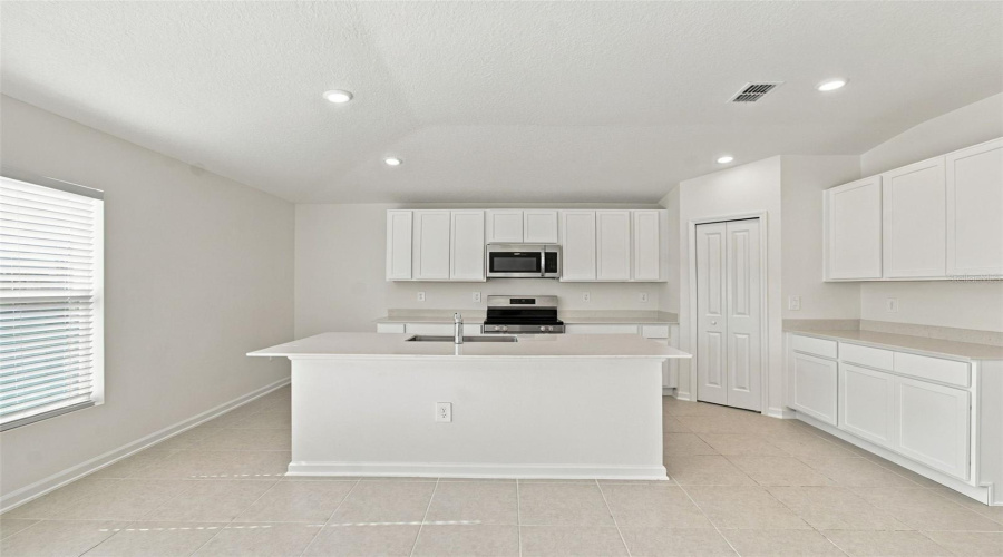 The Kitchen Offers A Spacious Island With Breakfast Bar, White Shaker-Style Cabinetry, And Quartz Countertops, All Overlooking The Dining And Living Areas.