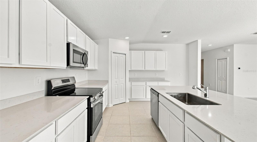 The Kitchen Offers A Spacious Island With Breakfast Bar, White Shaker-Style Cabinetry, And Quartz Countertops, All Overlooking The Dining And Living Areas.