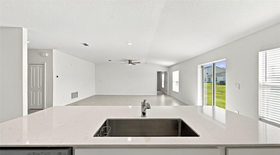 The Kitchen Offers A Spacious Island With Breakfast Bar, White Shaker-Style Cabinetry, And Quartz Countertops, All Overlooking The Dining And Living Areas.